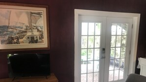 A room with a large window, a television on a wooden dresser, a trash can, and a chair.