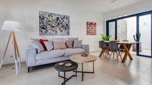 Un soggiorno moderno con un divano grigio, un tavolino rotondo e un'area pranzo con tavolo e sedie in legno. Alle pareti si trovano dipinti astratti e una grande finestra che fa entrare luce naturale.
