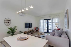 A modern living room with a white sofa, a dining table, and a TV mounted on the wall. - Homu Bianca - Villa with private pool (Playa Blanca (Yaiza))