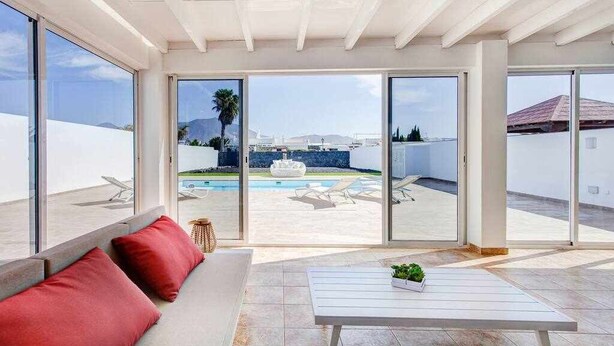 Un ampio balcone con un divano bianco, un tavolino con una pianta e vista su una piscina e montagne sullo sfondo.