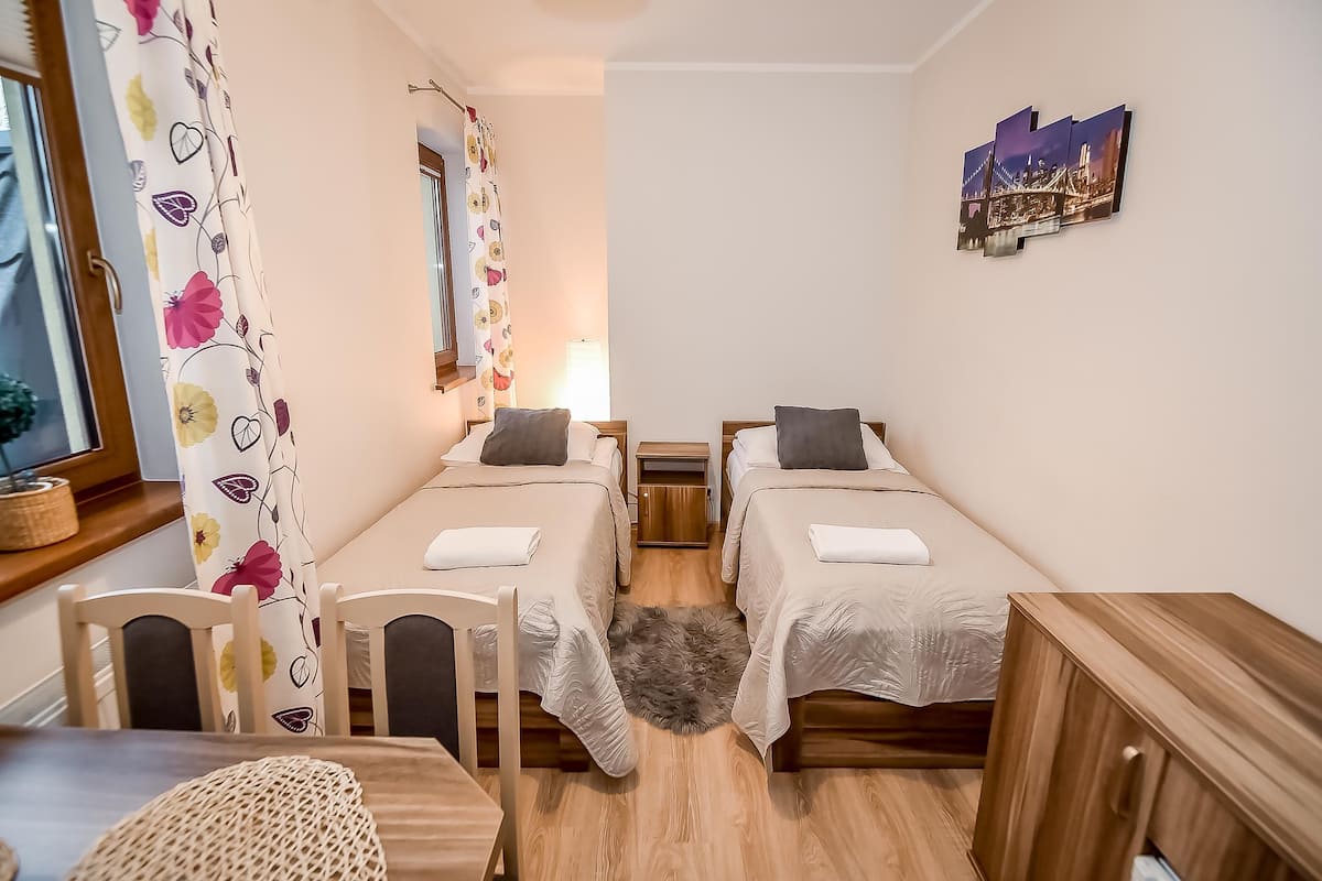A bedroom with two beds, a wooden desk, a chair, a mirror, and a wall-mounted picture.