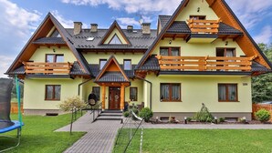 A two-story house with a steeply pitched roof, wooden balconies, and a well-maintained lawn. - Słoneczny Dworek (Bukowina Tatrzanska)