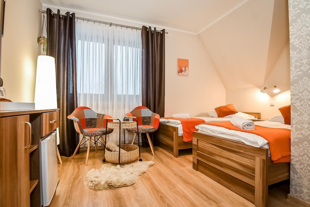 A cozy room with a bed, two chairs, a small table, a lamp, and a refrigerator.