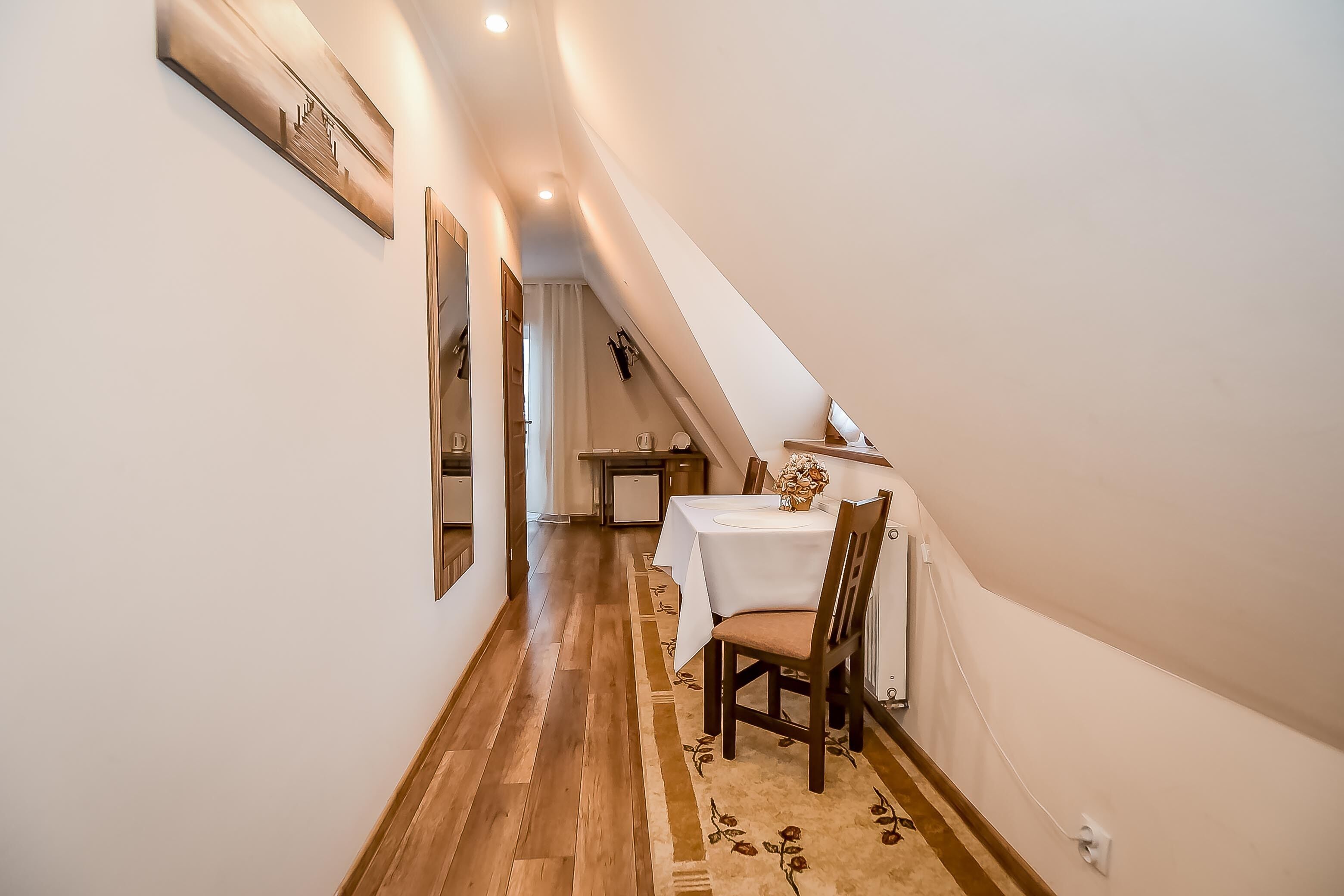 Ein schmaler Flur mit Holzdielen, ein Essbereich mit Tisch und Stühlen sowie eine Treppe, die zu einer oberen Ebene führt.