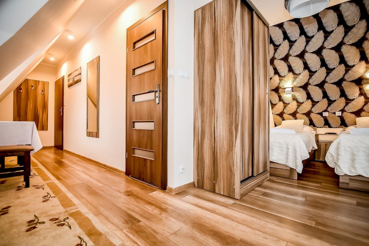 A modern hotel room with a wooden floor, a large wooden door, a patterned ceiling, and two beds with white linens.