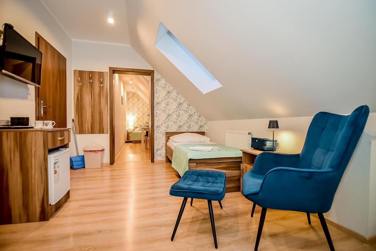 A compact room with a bed, a desk, a chair, a small fridge, and a skylight.