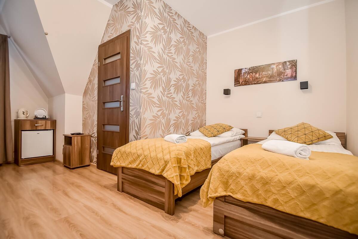 A bedroom with two beds, a wardrobe, a small cabinet, and a painting on the wall.