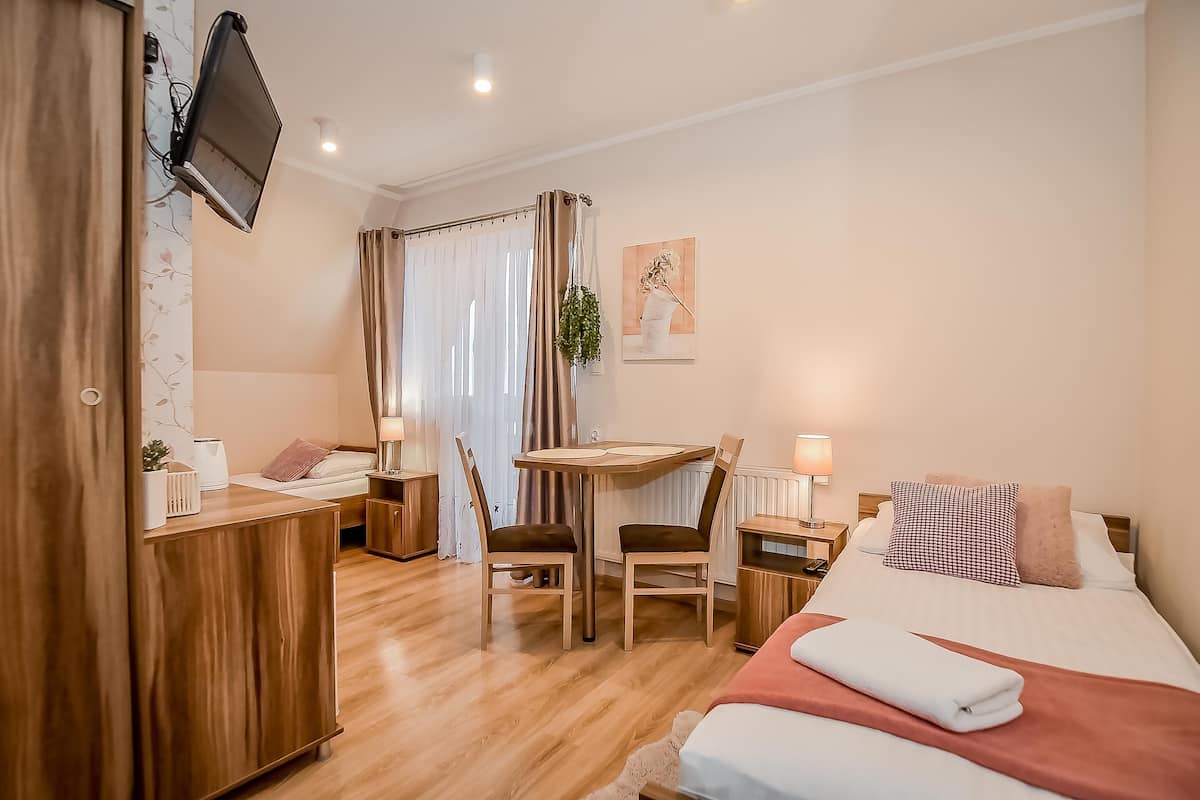 A hotel room with a bed, a desk, two chairs, a TV mounted on the wall, and a window with curtains.