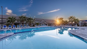 Schwimmbad mit Liegestühlen und Palmen, umgeben von Gebäuden.
