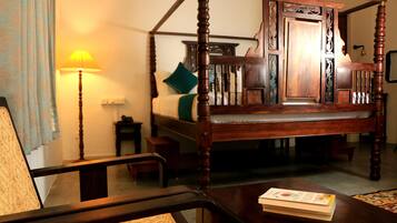 A traditional four-poster bed with a wooden headboard, a bedside table, a lamp, and a chair.