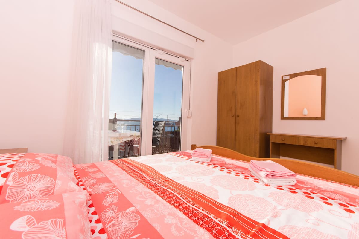A hotel room with a bed, a wooden wardrobe, a mirror, and a balcony with a view.