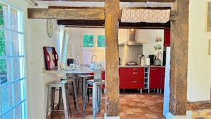 A kitchen with red cabinets, a stainless steel range hood, and a window overlooking greenery. - Gite l'Erisa (Annebault)