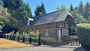 A traditional timber-framed house with a sloped roof, surrounded by a wooden fence and lush greenery. - Gite l'Erisa (Annebault)