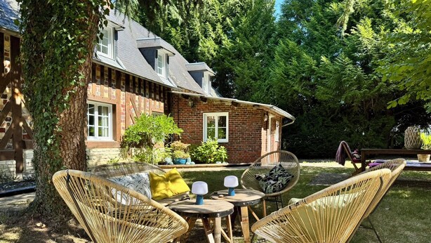 A rustic house with a brick exterior, a large tree in the yard, and wicker furniture. - Gite l'Erisa (Annebault)