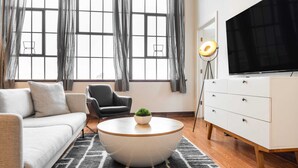 Ein stilvolles Wohnzimmer mit Sofa, Sessel, rundem Couchtisch, Fernseher und einer Lampe.