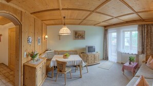 Ett mysigt rum med träväggar och träpanel i taket, ett matbord med stolar, en soffa, en tv och ett litet bord med en växt.