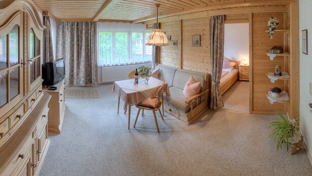 A cozy room with a wooden ceiling, a sofa, a table with a vase, and a television. - Ferienwohnung Apfelbaum 1. Etage, 42 qm, 1 Sep. Schlafzimmer, Balkon (Bad Feilnbach)