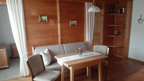 A cozy room with a wooden floor, a sofa, two chairs, a table with a vase of flowers, a hanging lamp, and a bookshelf. - Ferienwohnung Apfelbaum 1. Etage, 42 qm, 1 Sep. Schlafzimmer, Balkon (Bad Feilnbach)