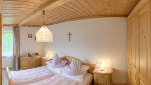 A bedroom with a wooden ceiling, a cross on the wall, a bed with two pillows, and bedside tables with lamps. - Ferienwohnung Apfelbaum 1. Etage, 42 qm, 1 Sep. Schlafzimmer, Balkon (Bad Feilnbach)