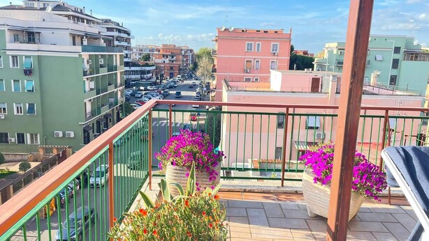 A balcony with a view of a city street, surrounded by buildings and potted plants with flowers. - Panoramic and Bright Penthouse is Waiting for you (Rome)