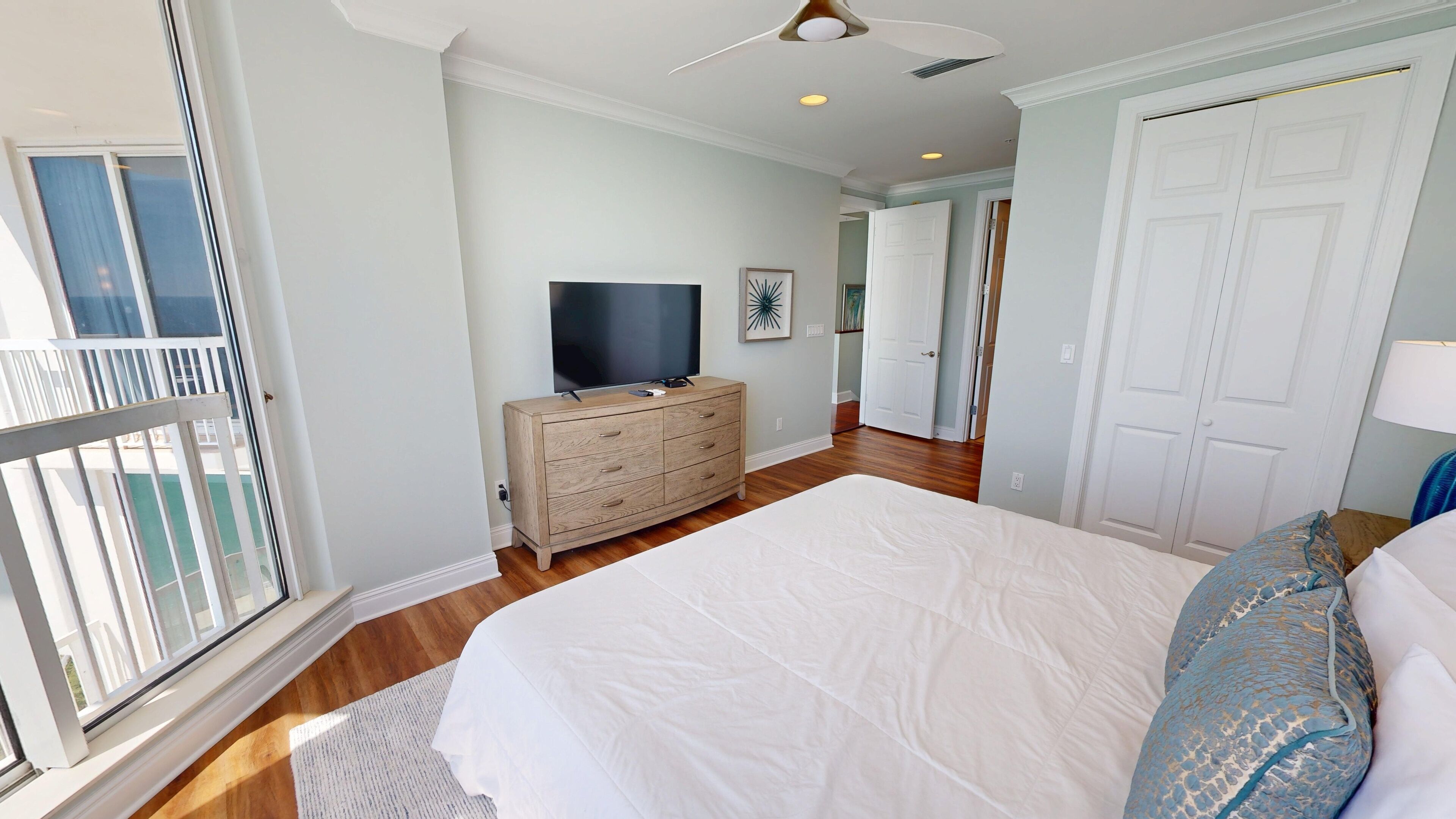 A bedroom with a large bed, a dresser, a television, and a door leading to another room.