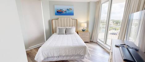 A bedroom with a bed, a nightstand, a lamp, a ceiling fan, and a large window with a view of the outside.