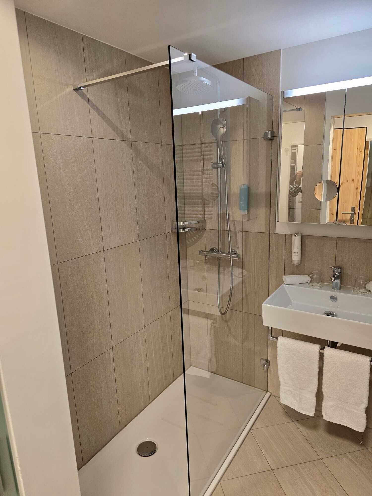 A modern bathroom with a glass-enclosed shower, a sink with a mirror, and a towel rack.