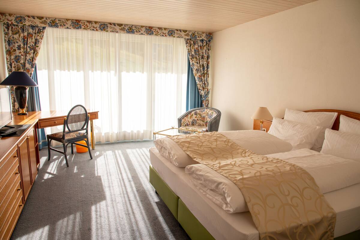 Een hotelkamer met een bed, een bureau, een stoel en een raam met gordijnen.