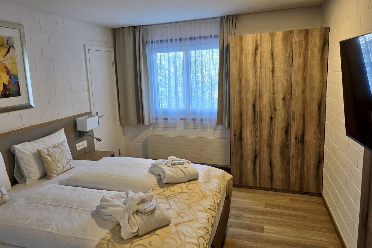 Een hotelkamer met twee bedden, een groot raam met gordijnen, een wandtelevisie en een schilderij aan de muur.