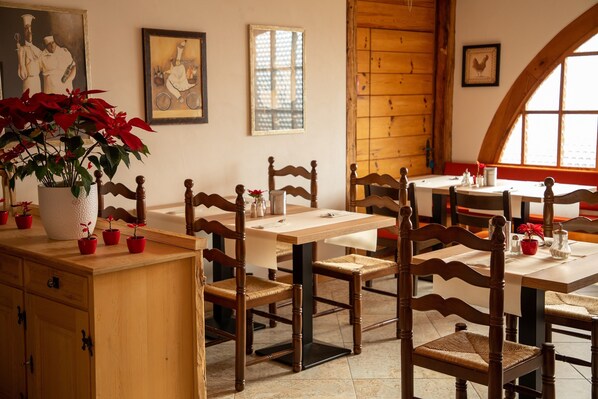 A dining area with wooden tables and chairs, a large potted plant, and framed pictures on the walls. - Alpenlodge Val Gronda (Obersaxen)