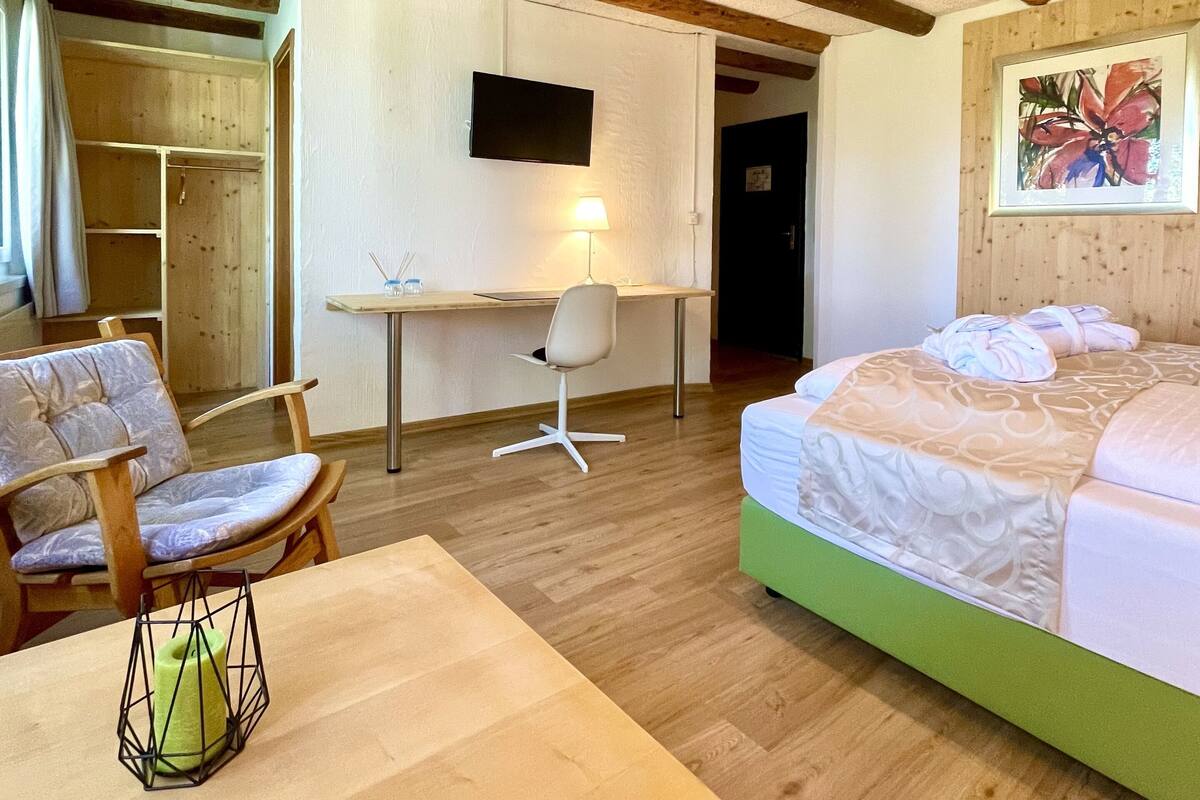 Een slaapkamer met een houten plafond, een bed met een groene hoofdeinde, een bureau met stoel en een televisie aan de muur.