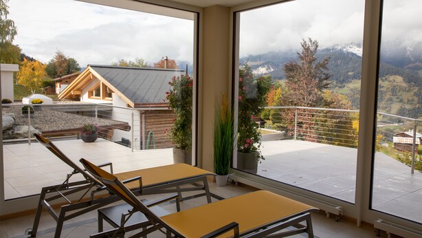 A modern room with large windows, a balcony, and a view of a mountainous landscape. - Alpenlodge Val Gronda (Obersaxen)