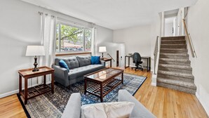 A living room with a grey sofa, two side tables with lamps, a glass coffee table, a patterned rug, and a wooden staircase. - Charming Arvada Home - Walking distance to Olde Town (Arvada)