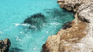 A coastal landscape with clear turquoise waters, rocky formations, and a distant sailboat. - Bella Horizonte - Beachfront 4 (Savaneta)