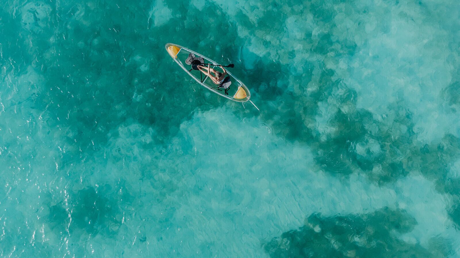 An aerial view of a clear turquoise sea with a single boat carrying two people.