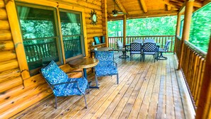 Eine Holzterrasse mit Tisch und Stühlen, umgeben von Holzwänden und großen Fenstern.