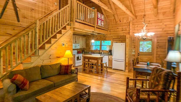 Ein gemütliches Blockhaus mit einer Holztreppe, einer Essecke, einer Küche und einem Wohnzimmer mit Sofa und Couchtisch.