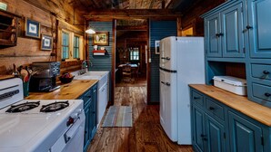 A rustic kitchen with wooden walls, a stove, a refrigerator, and blue cabinets.
