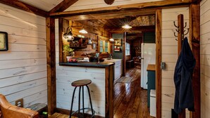 A rustic wooden interior with a bar area, wooden flooring, and a seating area with a leather chair.