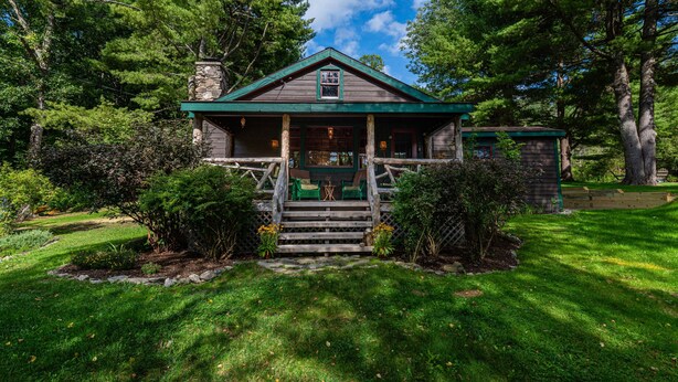 A rustic cabin with a stone chimney, wooden porch, and a small table and chair set outside.