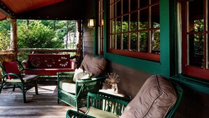 A porch with green wicker furniture, a bench, and a table with a vase.