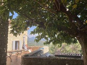 Un bâtiment en pierre doté d’une table et de chaises sur une terrasse, d’un mur en pierre et offrant une vue sur un paysage montagneux.