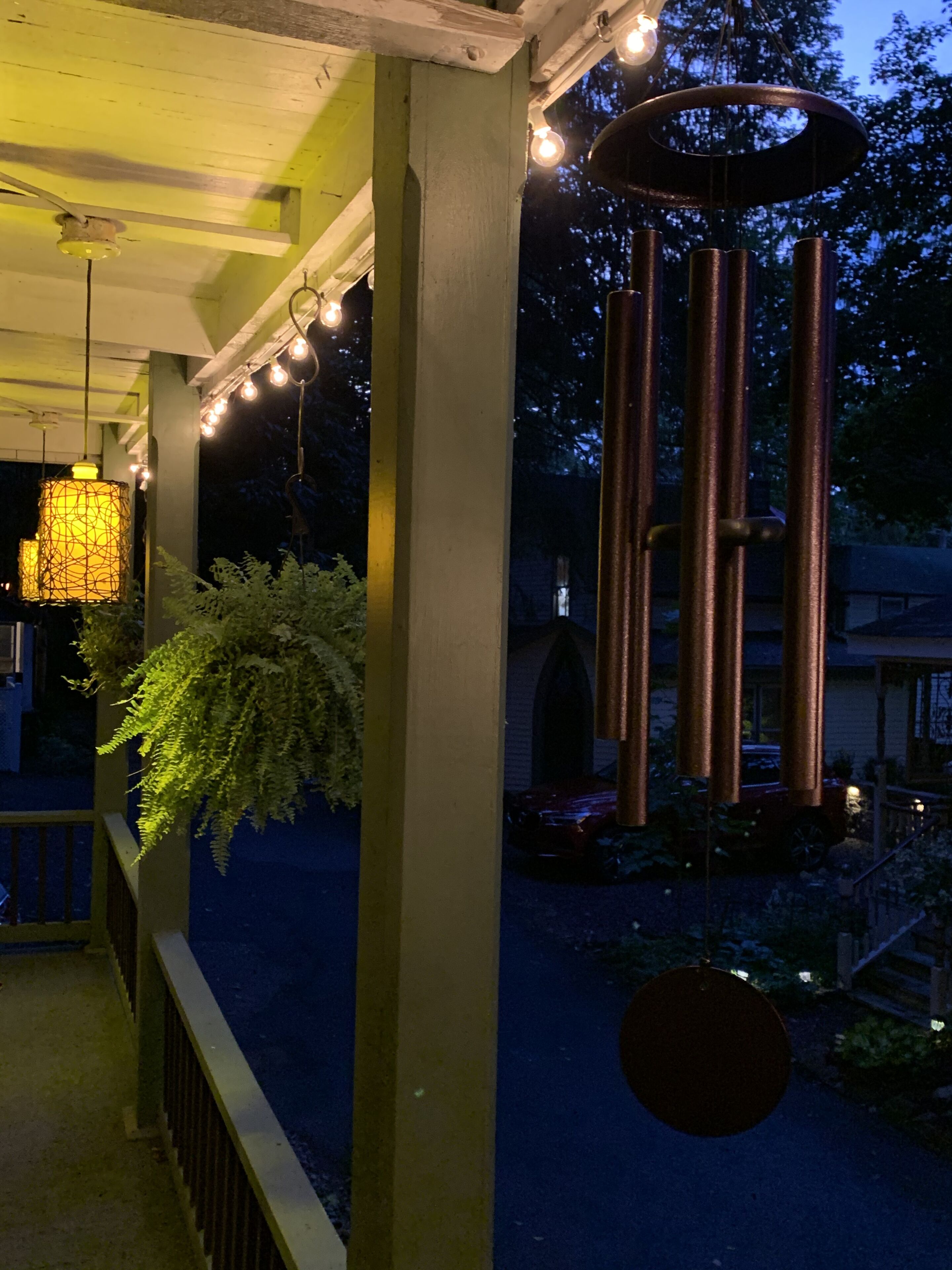 A covered outdoor area with a hanging light fixture, a wind chime, and a hanging plant.