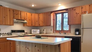 Une cuisine avec des meubles de rangement en bois, un îlot central, un four à micro-ondes, un réfrigérateur et un lave-vaisselle.