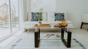 A modern living room with a glass coffee table, white sofa, and decorative pillows.