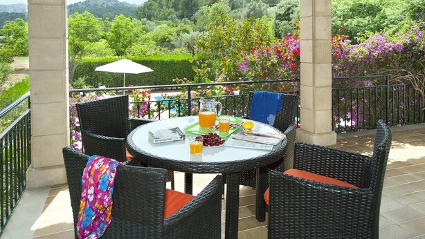 An outdoor patio with wicker furniture, a table with drinks and a book, and a view of greenery and mountains. - ROTGER. In Pollensa, just 800 m from the town centre! (Pollensa)