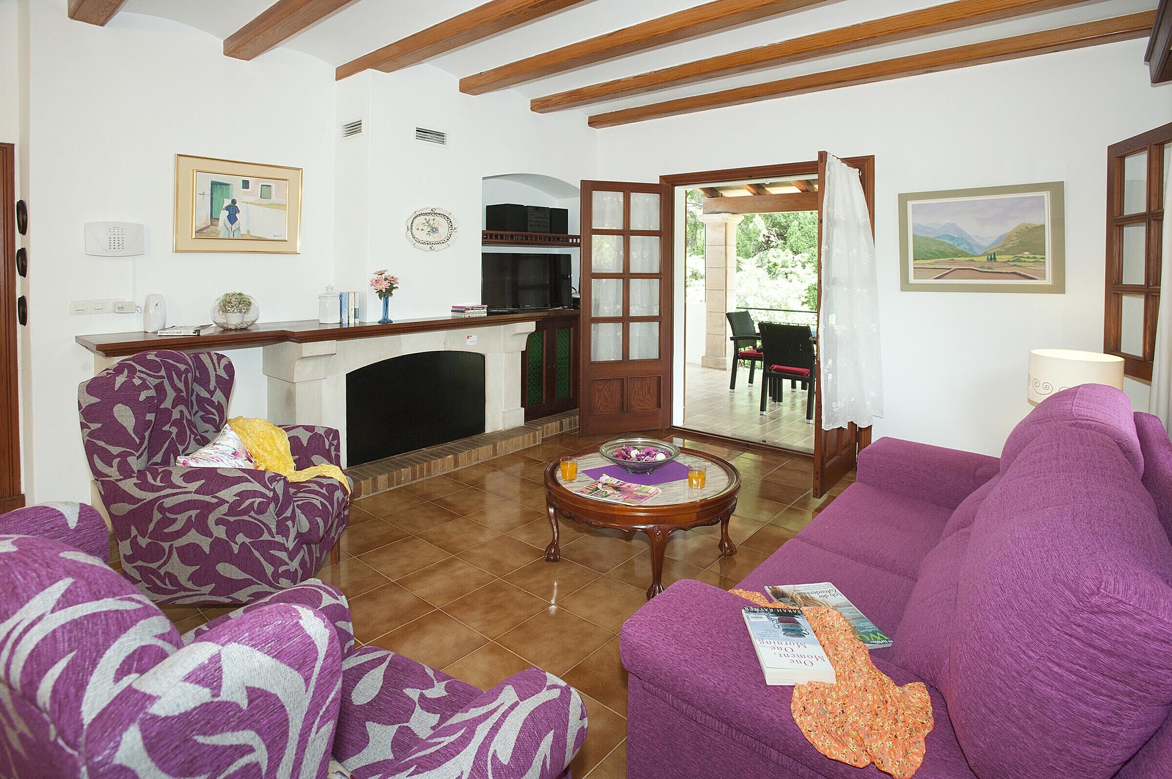 Una sala de estar con chimenea, sofás morados, una mesa de centro y vistas al exterior.