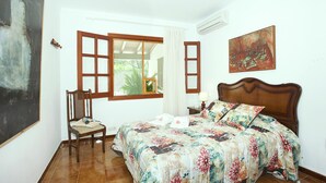 A bedroom with a wooden bed, a chair, a window with curtains, and a painting on the wall. - ROTGER. In Pollensa, just 800 m from the town centre! (Pollensa)
