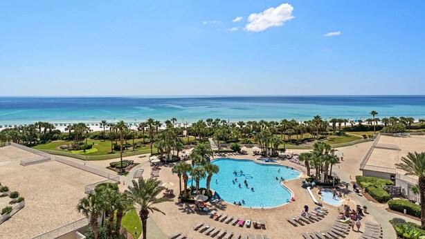 Un complexe hôtelier doté d’une grande piscine entourée de palmiers et donnant sur une plage.