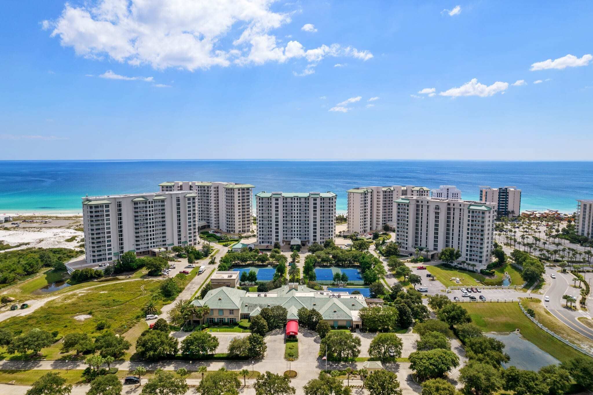 A high-rise hotel complex with multiple buildings, a central courtyard with pools, and a beach view.